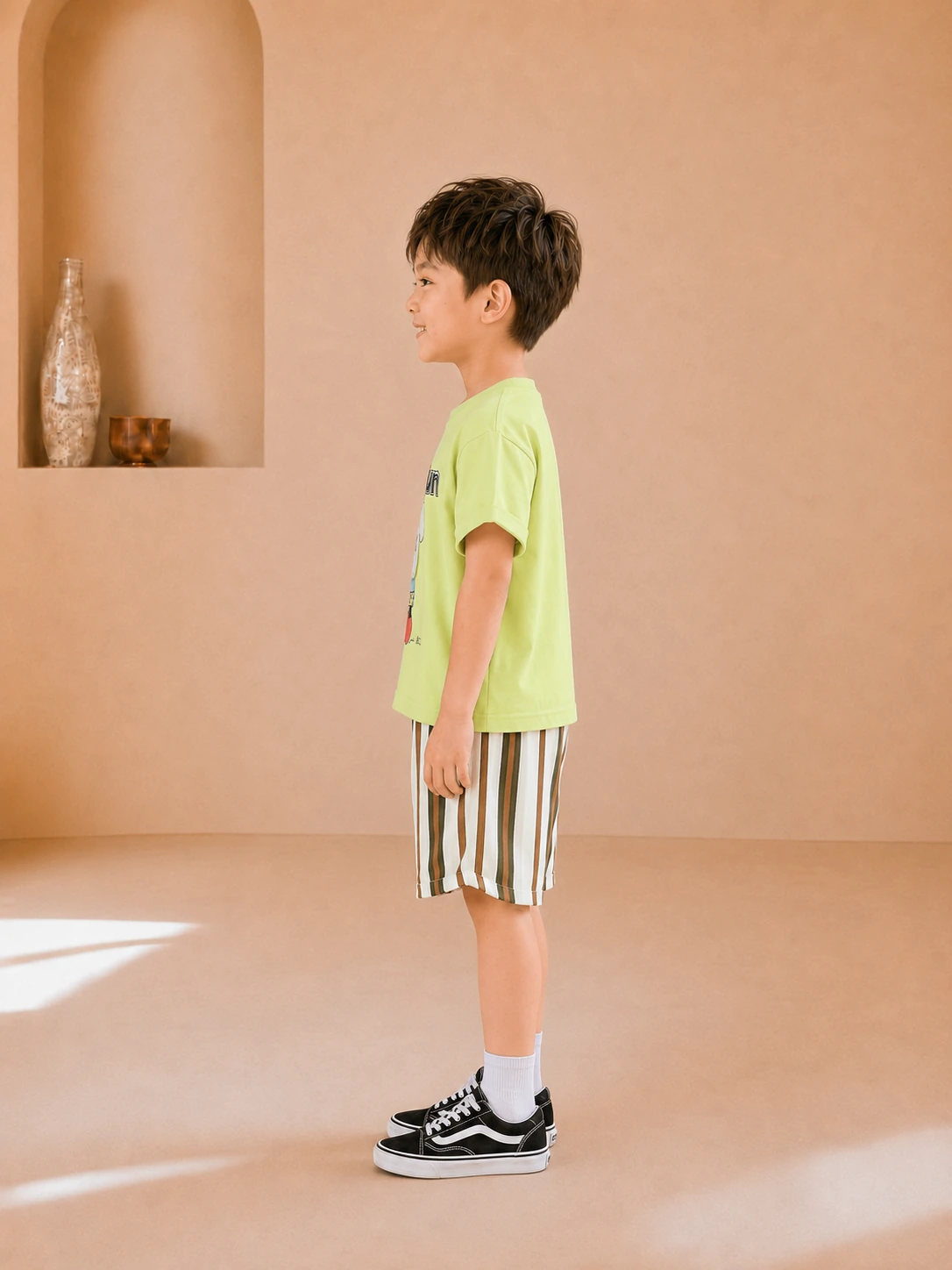 Boy wearing a lime green graphic T-shirt and striped knee-length shorts