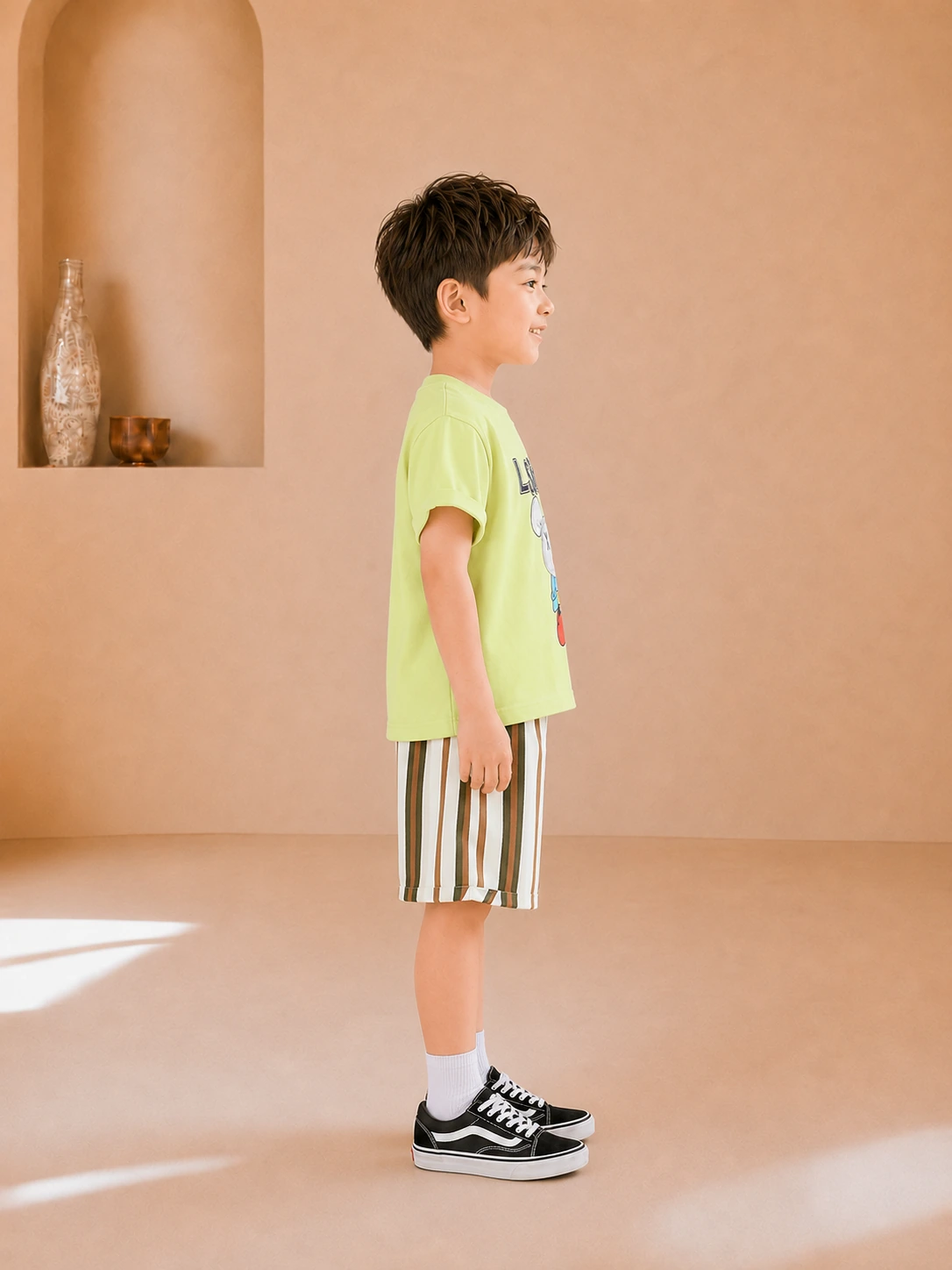 Boy wearing a lime green graphic T-shirt and striped knee-length shorts