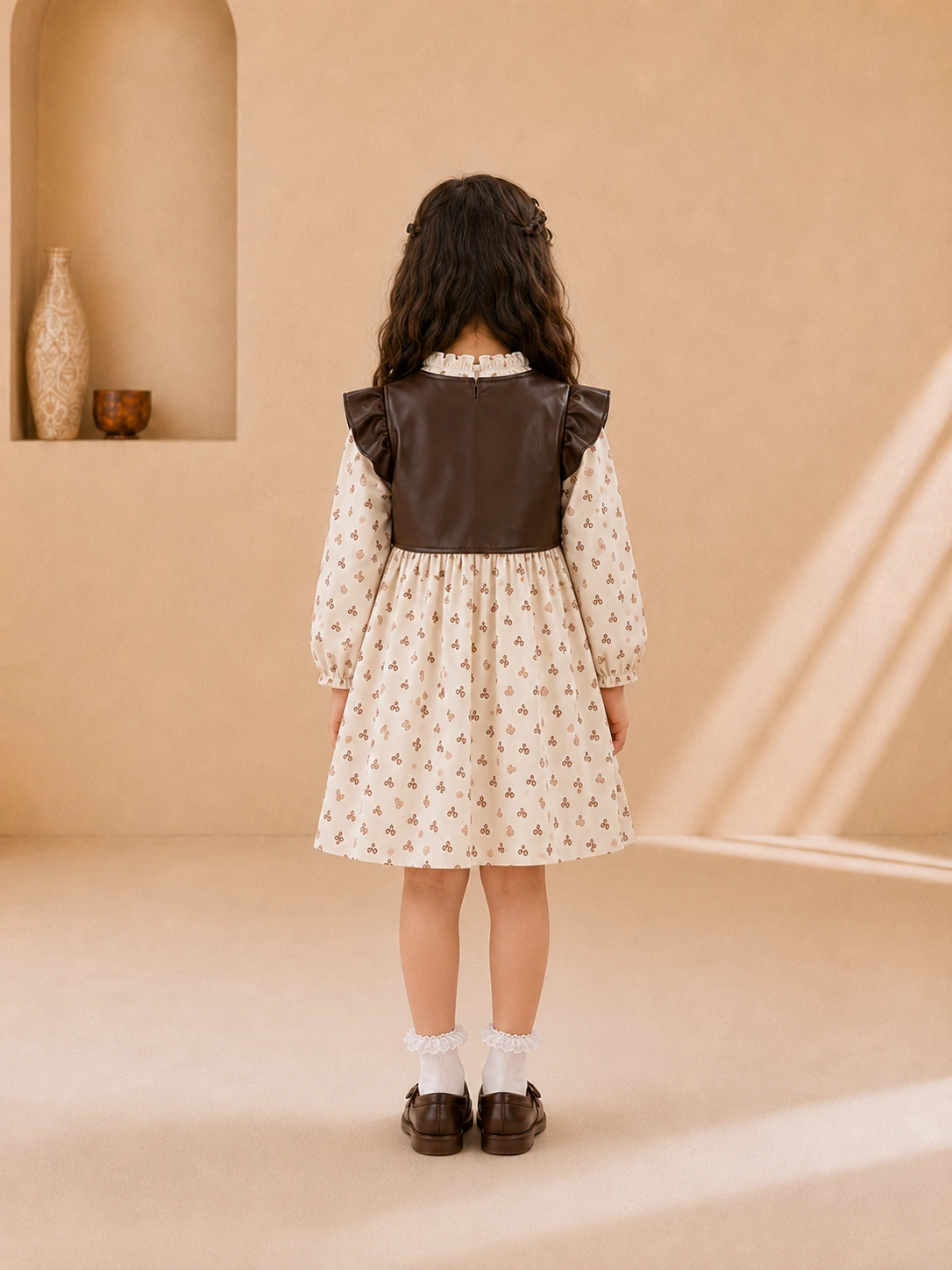 Girl wearing a cream printed long-sleeve dress with a brown faux-leather vest