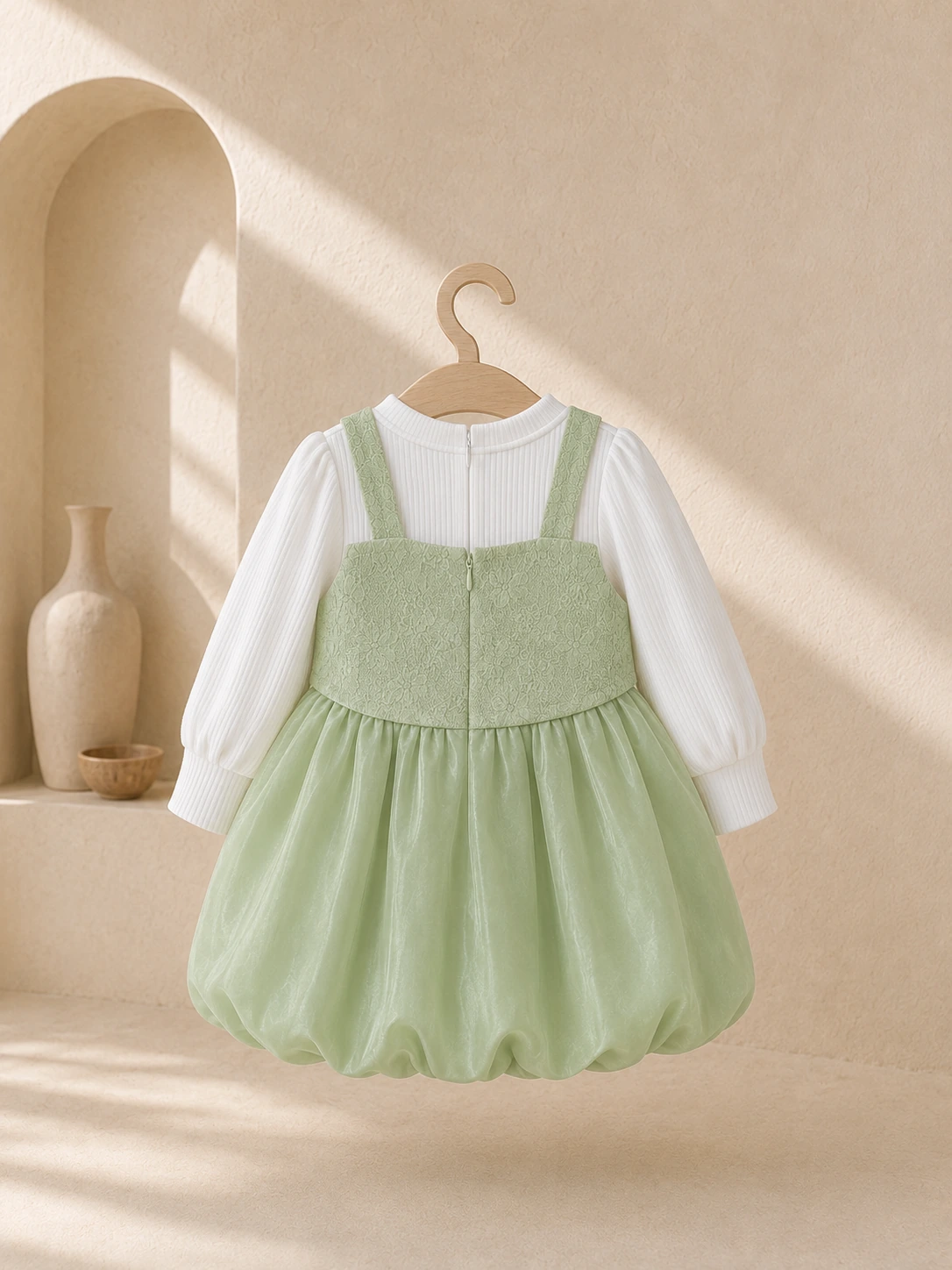 Girl wearing a green pinafore party dress with a white long-sleeve top