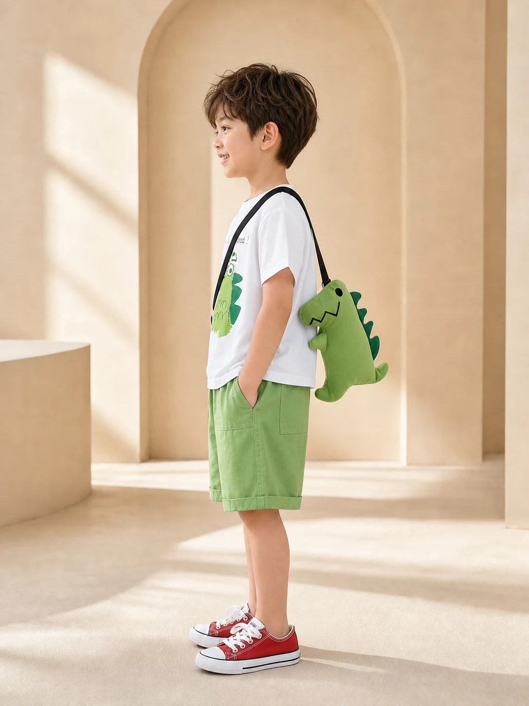 Boy wearing a white dinosaur T-shirt, green shorts and dinosaur crossbody bag