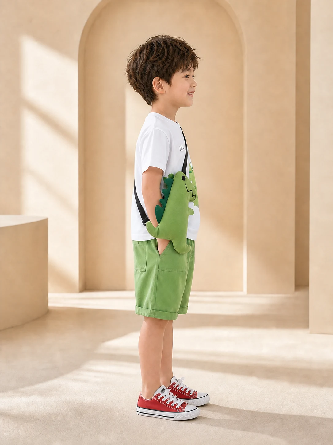 Boy wearing a white dinosaur T-shirt, green shorts and dinosaur crossbody bag