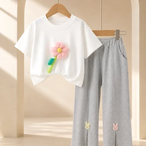 Girl wearing a white flower-appliqué T-shirt and grey ankle-length trousers
