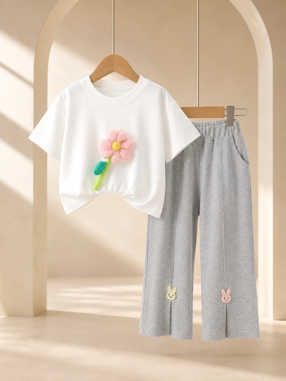 Girl wearing a white flower-appliqué T-shirt and grey ankle-length trousers