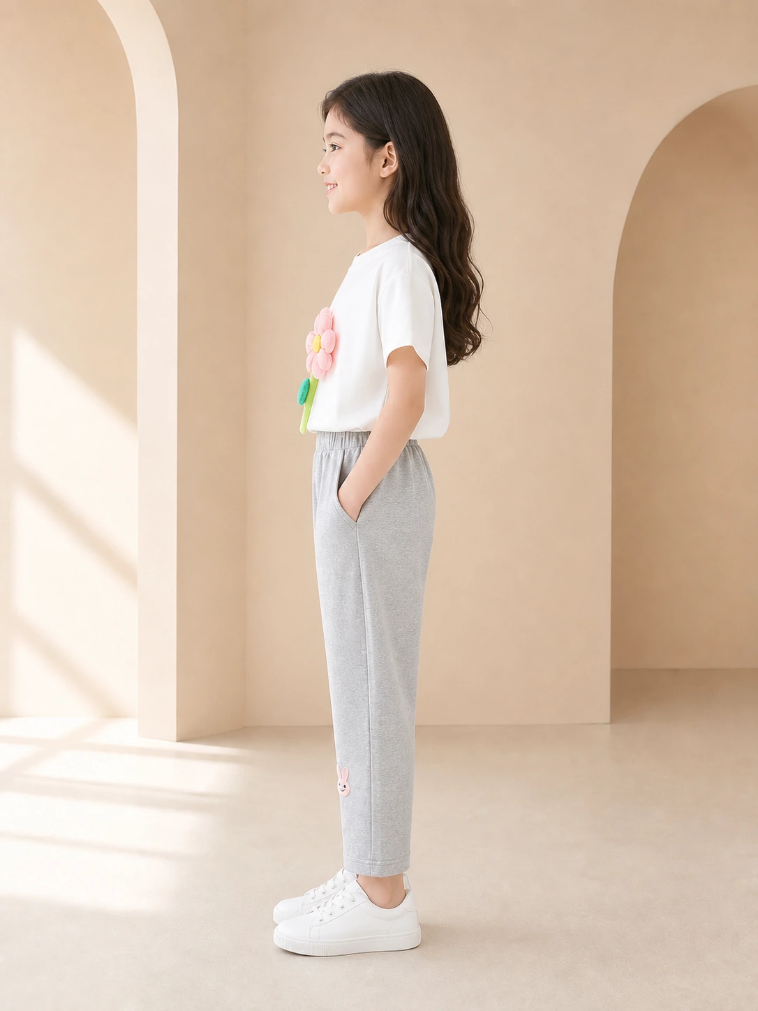 Girl wearing a white flower-appliqué T-shirt and grey ankle-length trousers