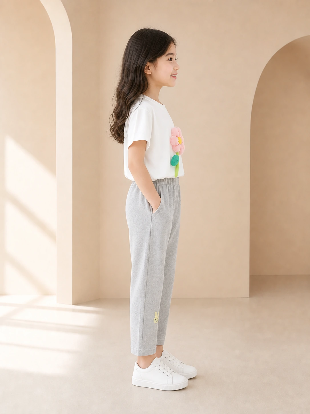 Girl wearing a white flower-appliqué T-shirt and grey ankle-length trousers